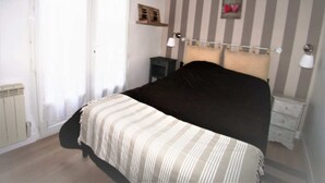 A bedroom with a bed, bedside tables, a radiator, a window, and striped wallpaper. - Résidence Les Althéas - Apartment 3 (Villers-sur-Mer)