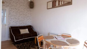 A cozy room with a brick wall, a brown sofa, a round table with papers, and a mirror reflecting a fence. - Résidence Les Althéas - Apartment 3 (Villers-sur-Mer)