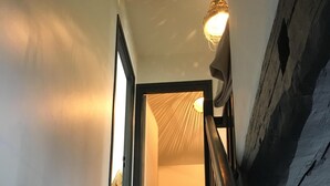 A staircase with wooden steps and a black handrail, leading to a room with a white ceiling and a hanging light fixture. - CHARMING 4 **** in quiet, fully renovated, near the sea - PMR (Santec)