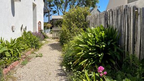 A narrow gravel path leading to a white building with a wooden fence and lush greenery. - CHARMING 4 **** in quiet, fully renovated, near the sea - PMR (Santec)