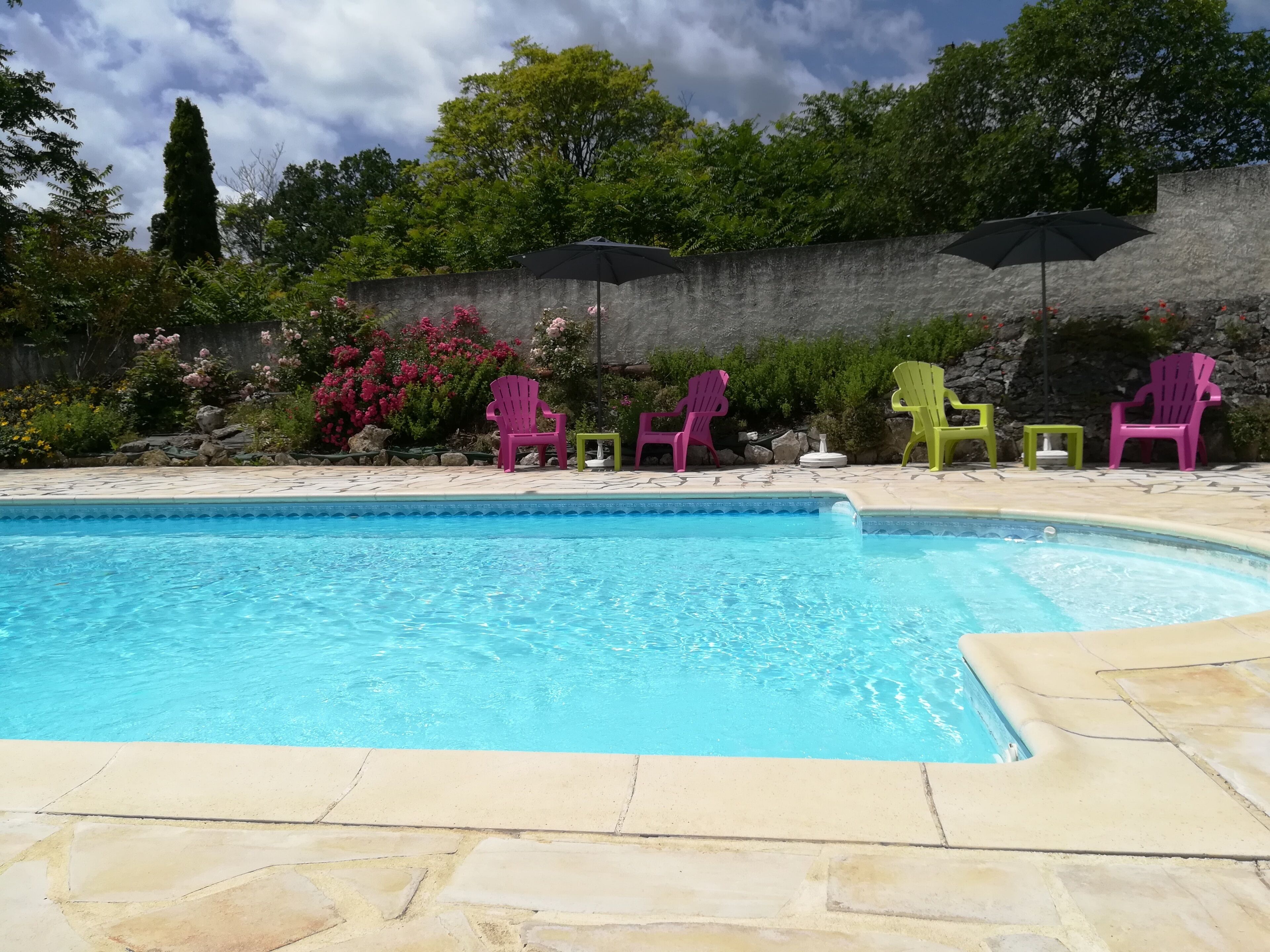 A swimming pool with a stone deck and colorful Adirondack chairs.