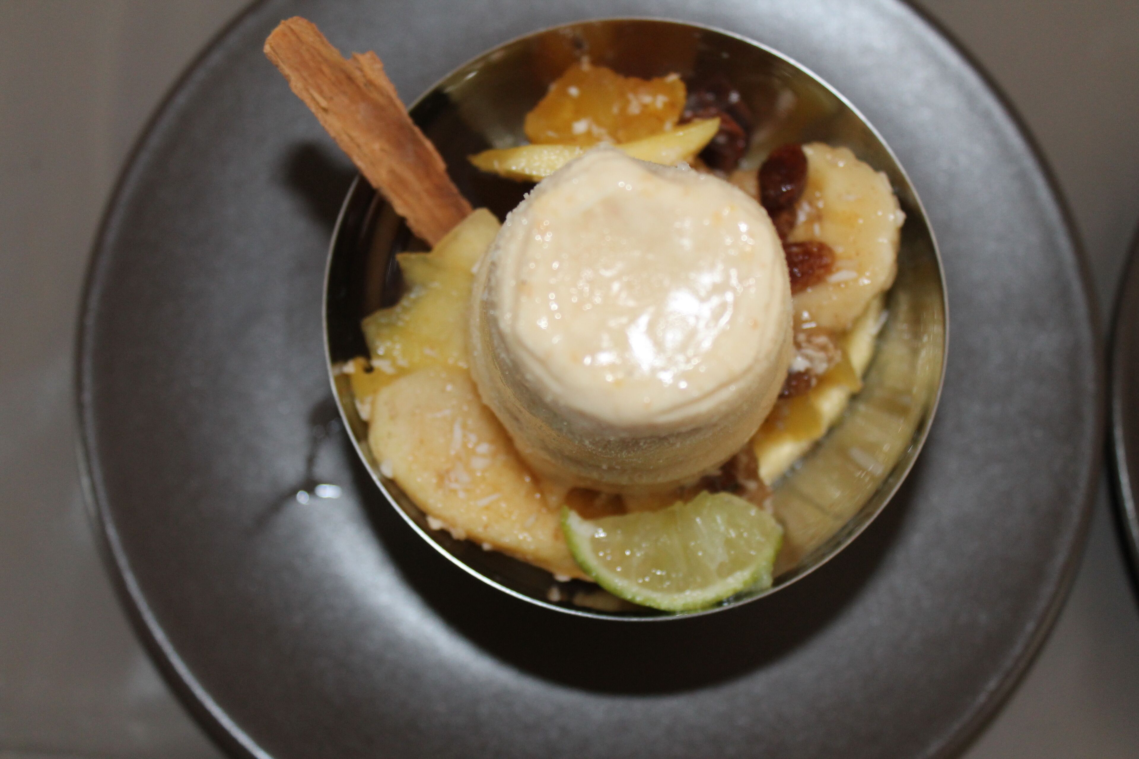 Ein Dessert in einer Metallschüssel mit Zimtstange, Ananas und Limette.