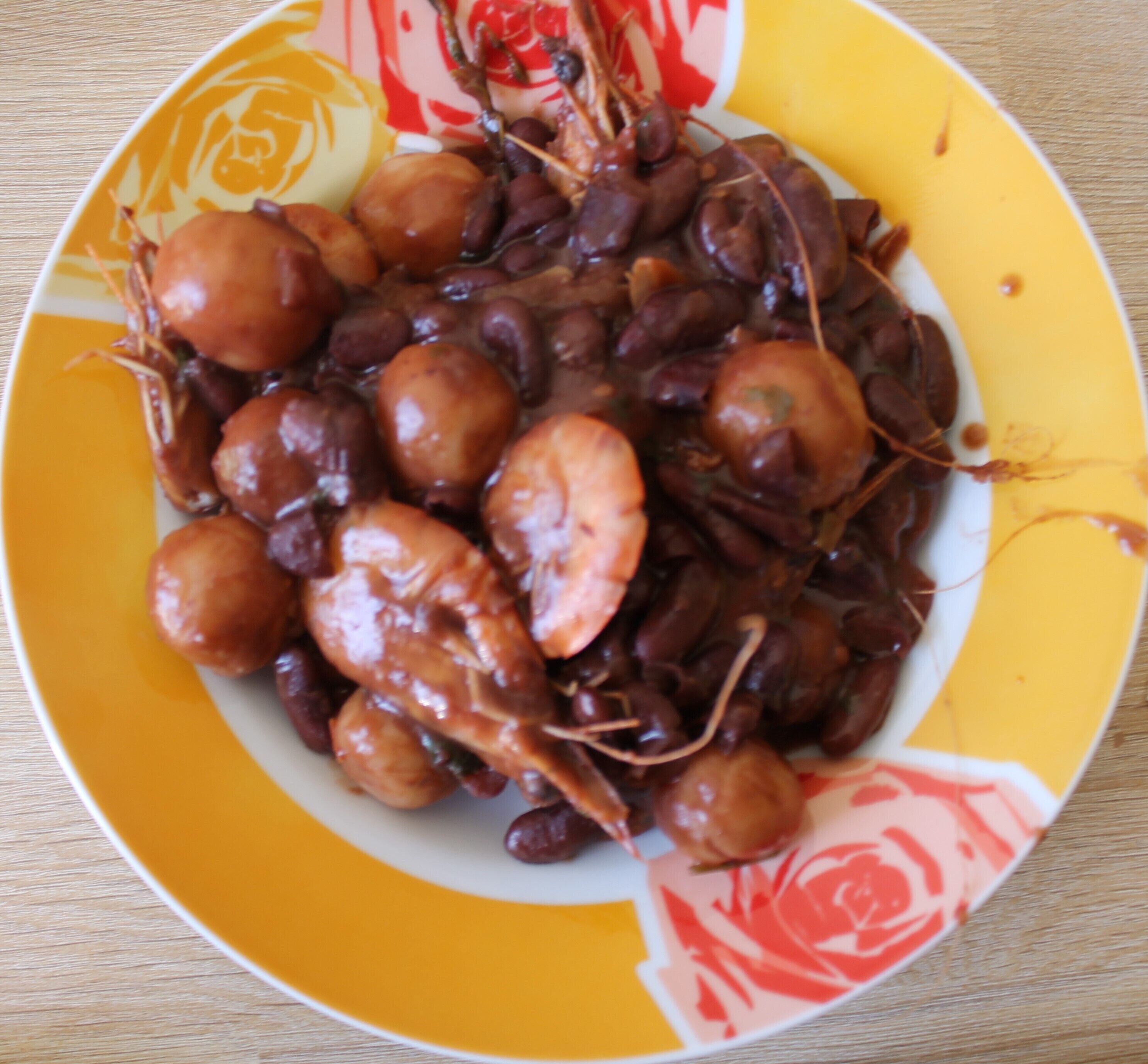A plate of cooked seafood, including shrimp and beans, on a yellow plate with a floral design.