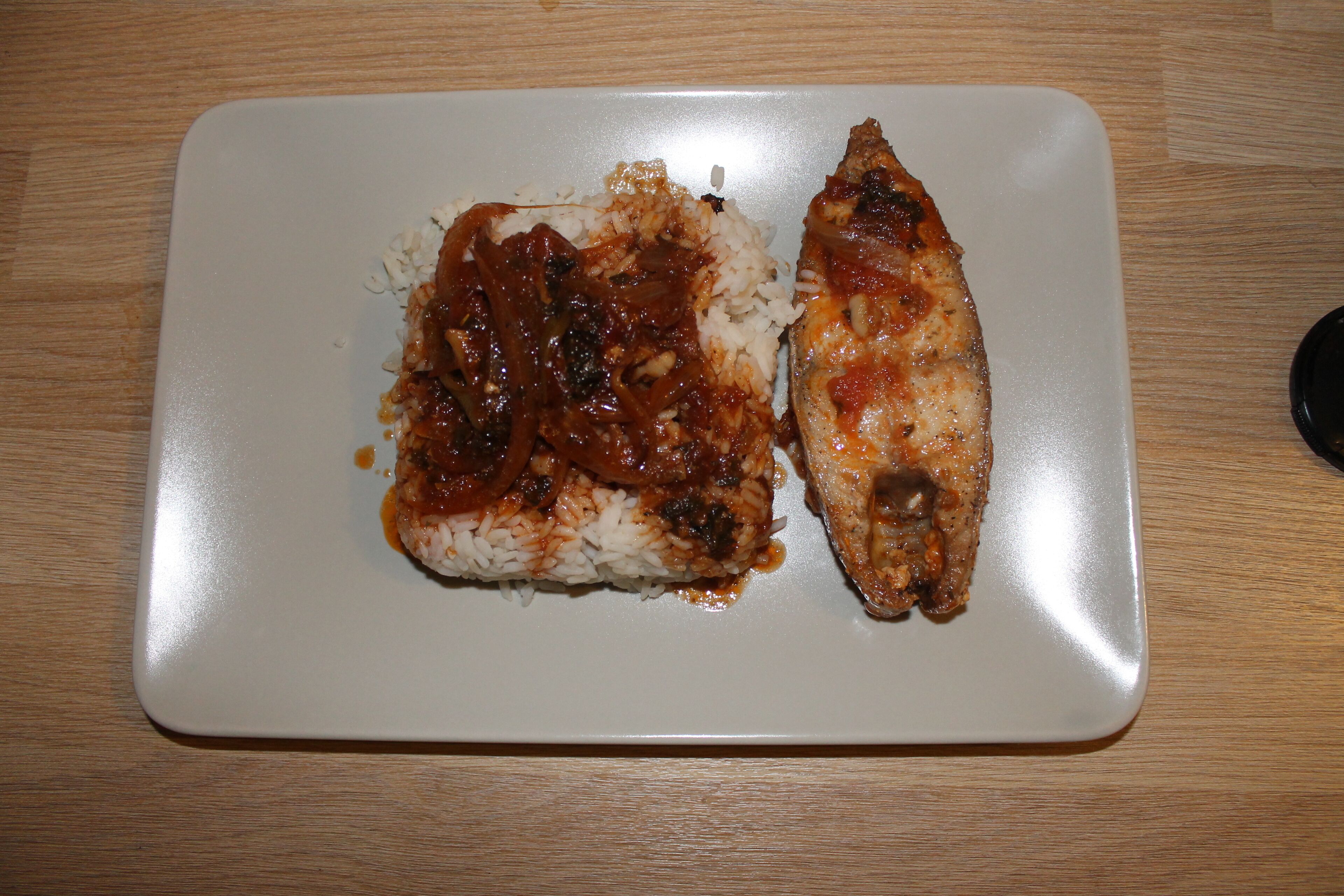 Ein weißer Teller mit gegrilltem Hähnchen und Reis auf einem Holztisch.
