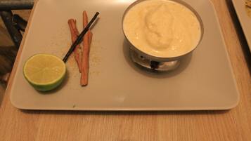A white plate with a bowl of creamy dip, a lime wedge, and two sticks of cinnamon on a wooden table.