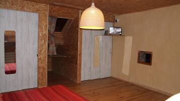 A room with a wooden ceiling, a bed with a red and white striped bedspread, a hanging light fixture, and a small television on a shelf.