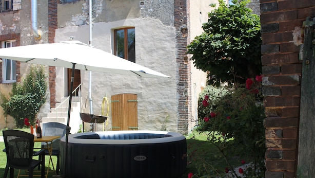 Un bain à remous dans un jardin, avec une table et des chaises, entouré d’un mur de briques et d’un jardin où poussent des rosiers.
