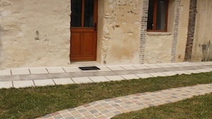 Un bâtiment doté d’une porte et d’une fenêtre en bois, d’un chemin pavé et d’une zone herbeuse.