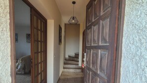 Un couloir avec un sol carrelé, une porte en bois et un escalier menant à une autre pièce.