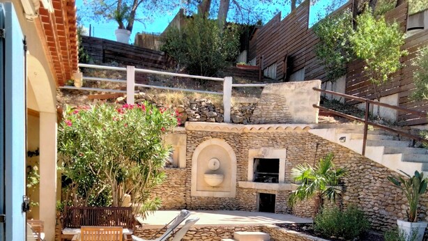 A patio area with a stone wall, outdoor seating, and a small fire feature. - Large villa with pool in Provence near Les Baux de Provence, Nimes (Beaucaire)