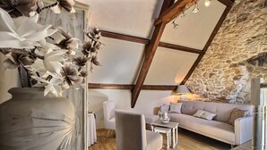 A cozy room with a stone wall, a wooden ceiling, a sofa, a chair, and a large vase with flowers.