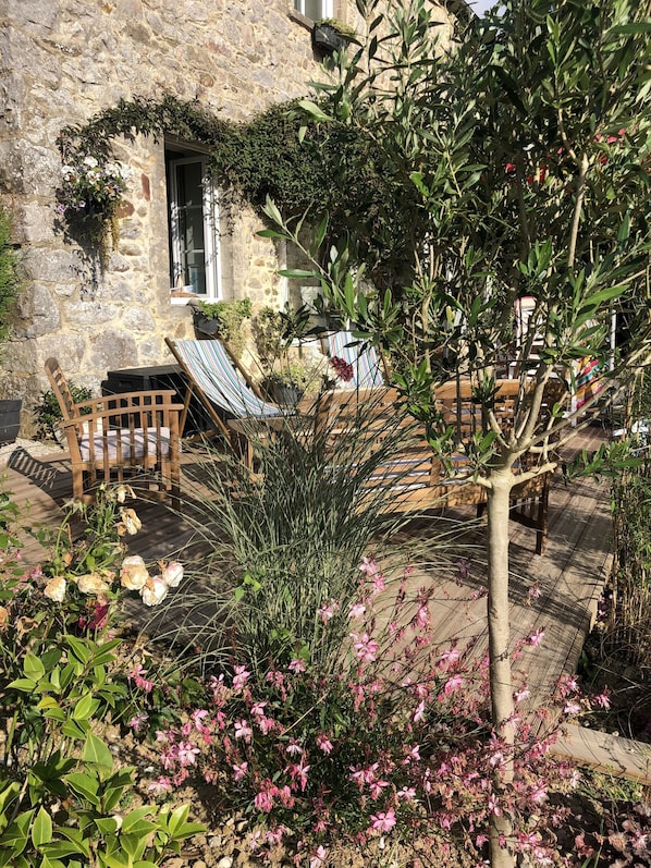 A stone building with a wooden deck, outdoor seating, and flowering plants.