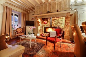 Un salon chaleureux avec une cheminée, des poutres apparentes, un téléviseur et des sièges confortables.
