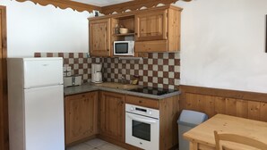 Een compacte keuken met houten kastjes, een magnetron, een koffiezetapparaat, een spoelbak en een kleine oven.