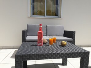 Een betegelde buitentafel met een fles Saint James, twee glaasjes sinaasappelsap en een peer.