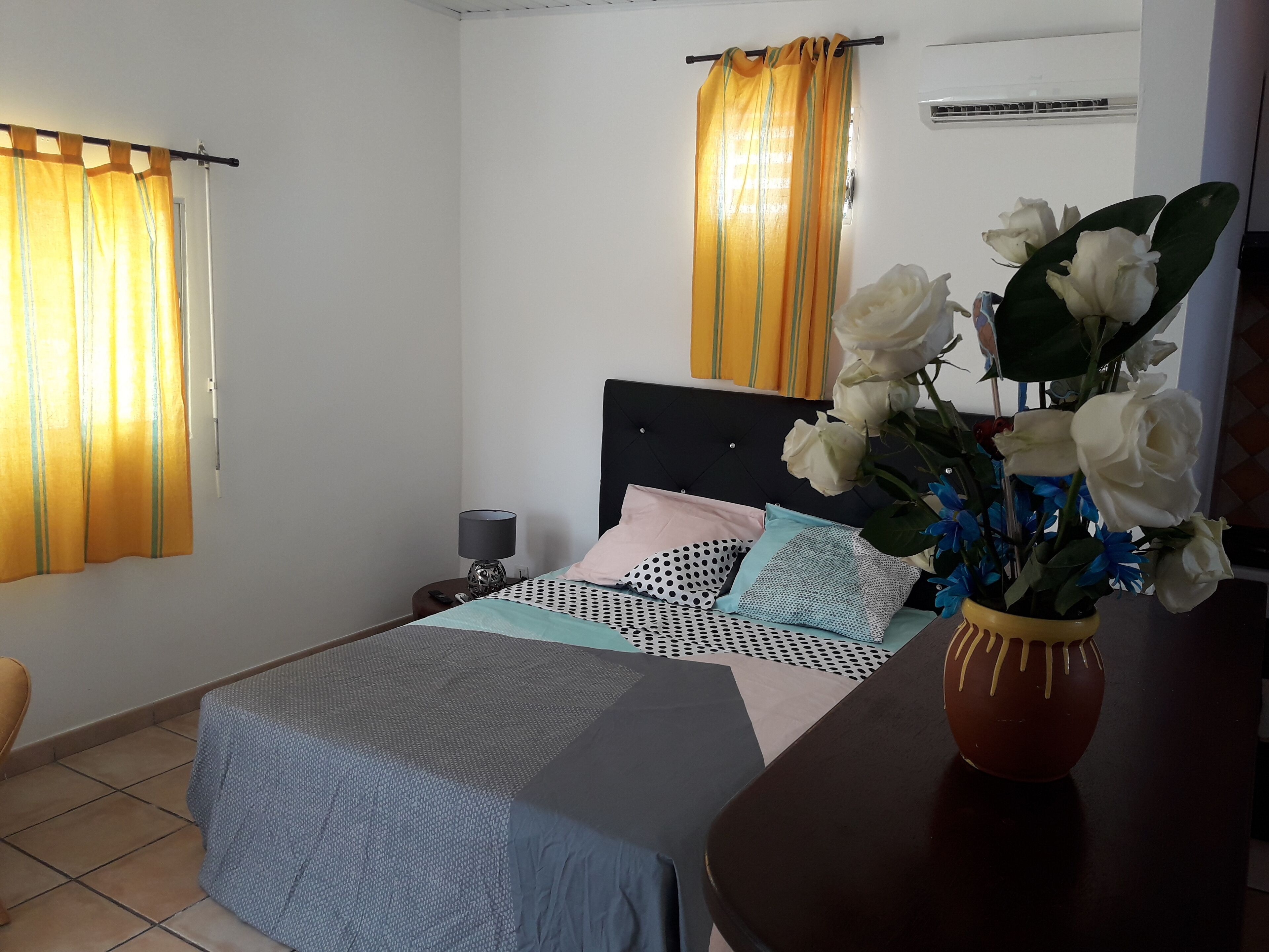 A bedroom with a bed, a nightstand, a lamp, a vase with flowers, and curtains.