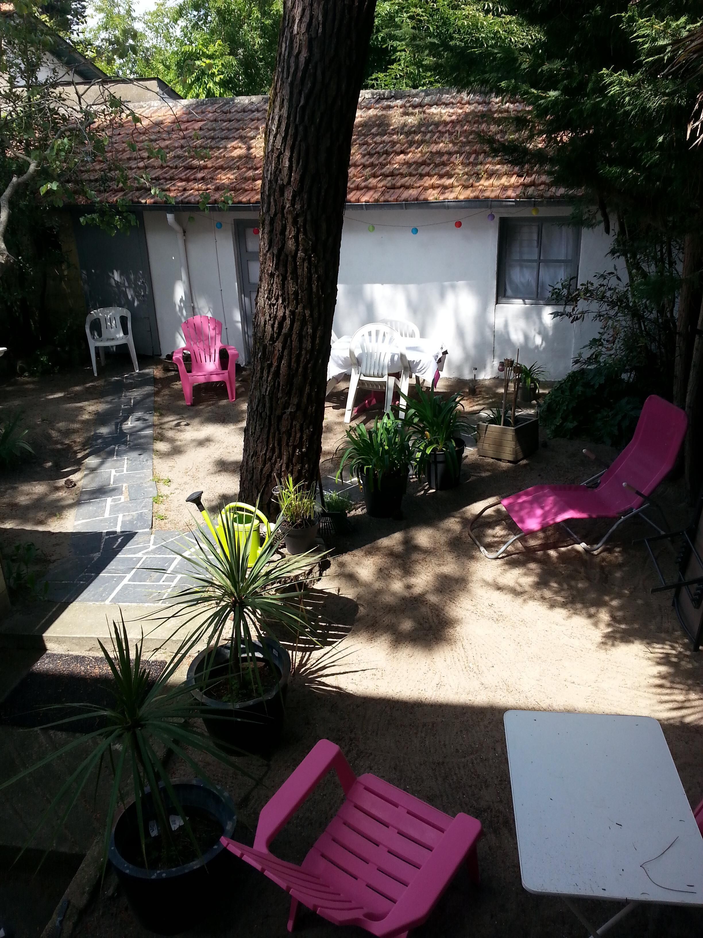 Un patio con techo de baldosas, plantas en macetas y mobiliario exterior, incluyendo sillas y una mesa.