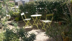 A courtyard with a table and chairs, surrounded by potted plants and a stone building in the background.