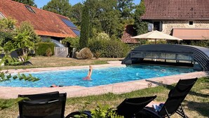 Una piscina con sillas de descanso, una zona cubierta y una casa con techo de tejas.