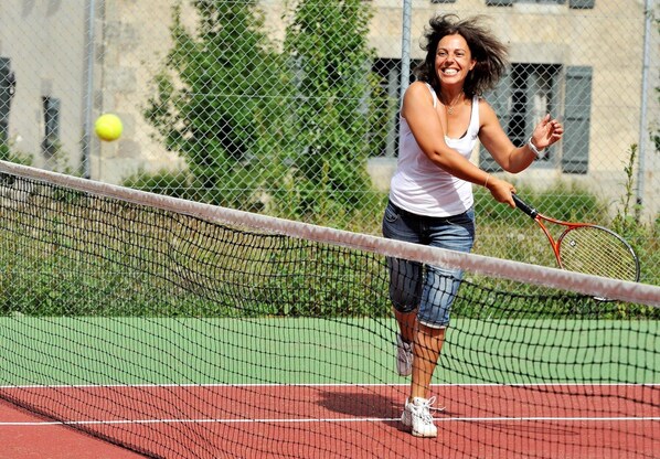 A tennis court with a net, a player in a white tank top and denim shorts, and a tennis racket.