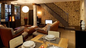 Una sala de estar acogedora con chimenea, sofás de cuero, una mesa de comedor preparada para cuatro personas y una escalera de piedra.