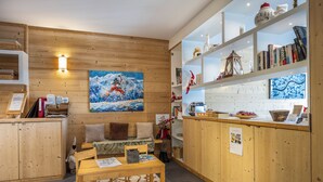 A cozy room with wooden walls, a painting of a snowy mountain, a wooden table, and a bookshelf with books and decorative items. - 110m² apartment, full services 4 *, 3 bedrooms, 3 bathrooms / d, south balcony and 2 parking spaces (Montvalezan)