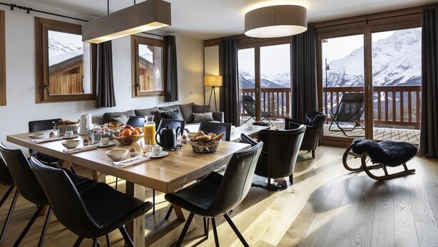 A modern dining area with a wooden table, black chairs, and a view of snow-capped mountains through large windows. - 110m² apartment, full services 4 *, 3 bedrooms, 3 bathrooms / d, south balcony and 2 parking spaces (Montvalezan)