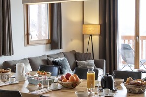 Un salon chaleureux avec un canapé, une table basse sur laquelle sont disposés des éléments pour le petit-déjeuner, une lampe et une vue sur l’extérieur.