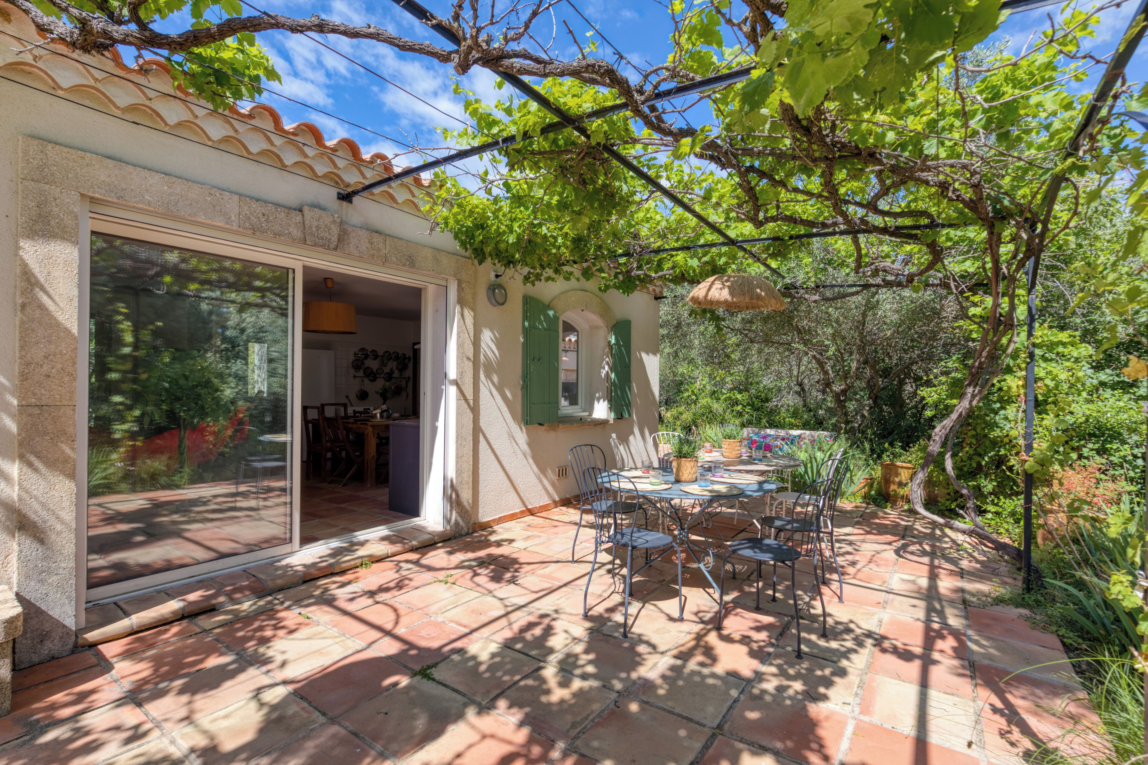 A patio with a table and chairs, a sliding glass door, and a garden area with trees and plants.