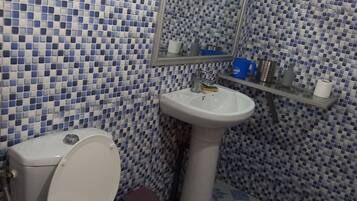 Une salle de bain avec des toilettes, un lavabo et un miroir. Les murs sont recouverts de carreaux bleus et blancs.