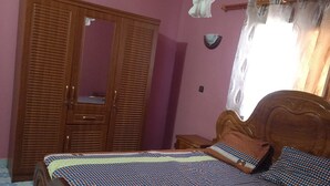 A bedroom with a bed, wooden wardrobe, and a ceiling fan.