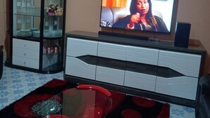 A living room with a television on a stand, a glass cabinet with decorative items, and a red and black patterned coffee table.