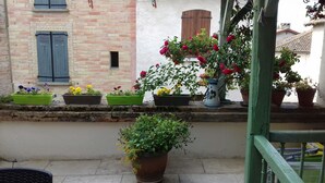 Ein Balkon mit Blumentöpfen und Blumen, eine Ziegelwand und ein Fenster mit Rollläden.