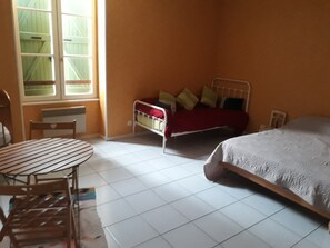 Ein Schlafzimmer mit Bett, Sessel, Tisch und Fenster.