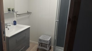 Ein Badezimmer mit einem weißen Waschbecken, einem kleinen Korbsitz und einer Duschkabine.