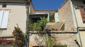 Eine schmale Gasse mit Gebäuden im traditionellen Stil, darunter eine sichtbare Türnummer 3 und ein kleiner Balkon mit Blumentöpfen.