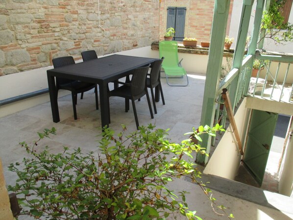 Eine Terrasse im Freien mit Tisch und Stühlen, einem grünen Sessel, Topfpflanzen und einer Steinmauer.