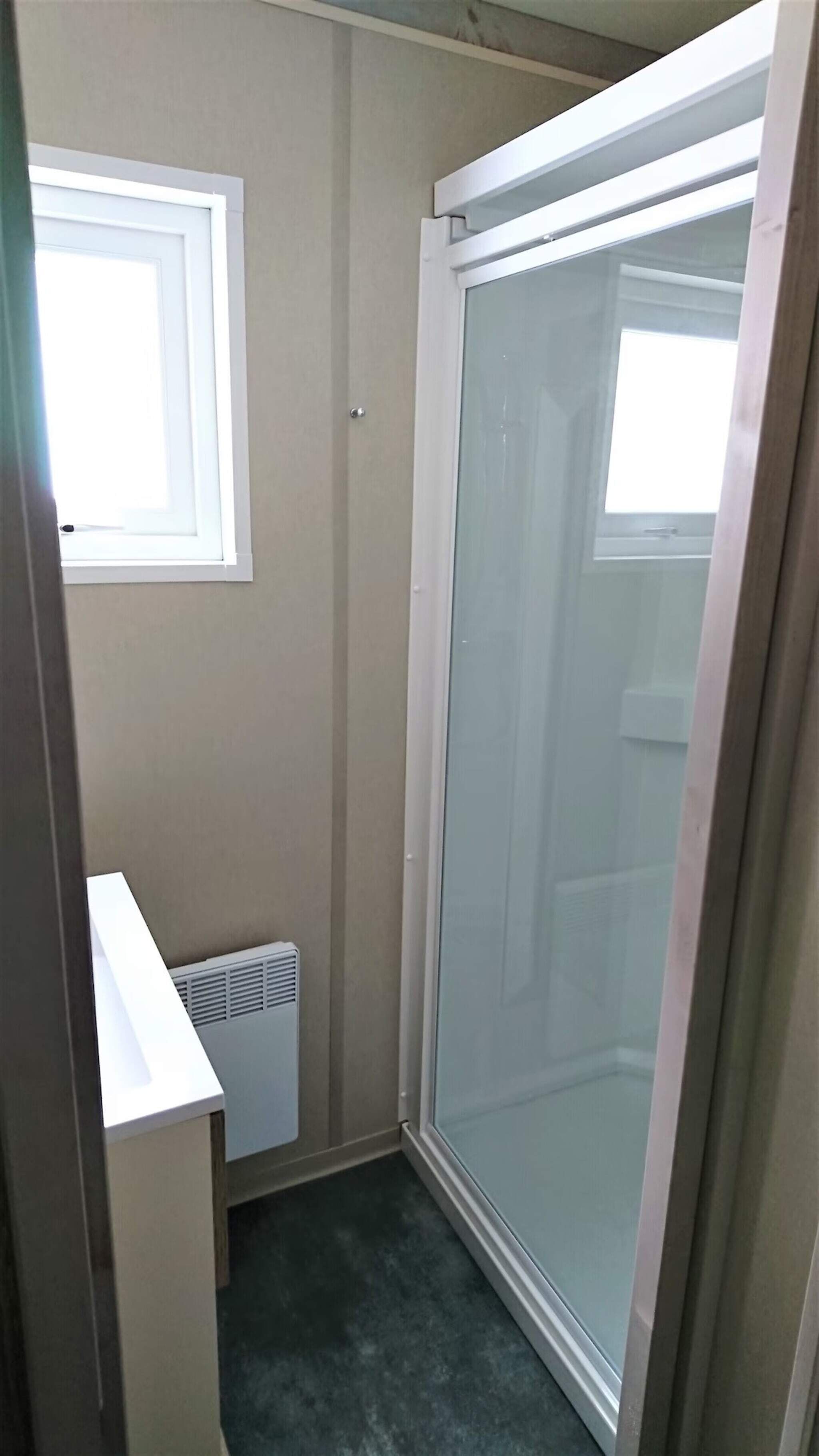 Een kleine, smalle kamer met een raam, een radiator en een schuifglasdeur.