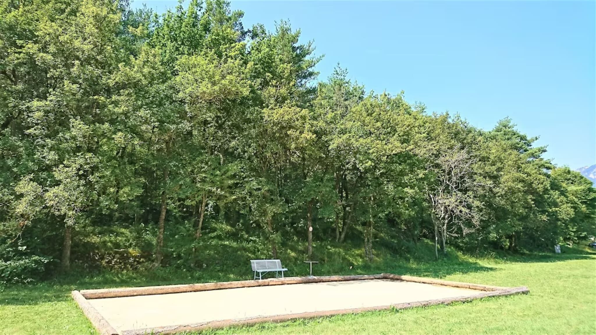 Une zone herbeuse avec un banc en bois et un panneau, entourée d’arbres verdoyants et touffus.
