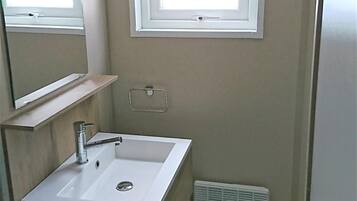 Un bany petit amb un lavabo blanc, un mirall, una finestra i una sortida d'aire.