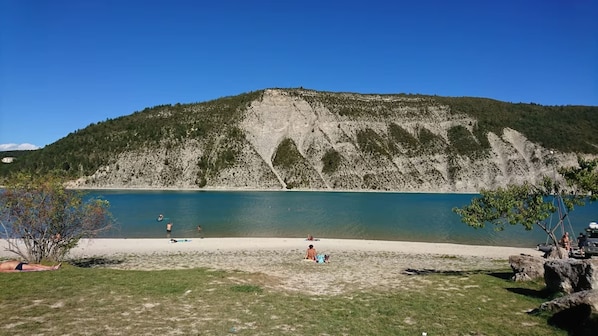 A beach with clear blue water, a grassy foreground, and a rocky hill in the background.