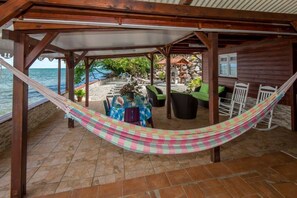 A covered outdoor area with a hammock, a table with chairs, and a view of the sea. - the feet in water (le francois)