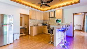 Una cocina moderna con armarios de madera, un refrigerador de acero inoxidable, horno empotrado, cafetera y una barra con taburetes.