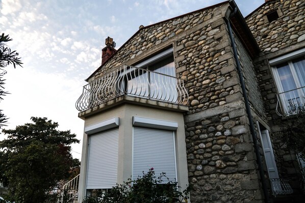 A stone building with a balcony, shutters, and a chimney.