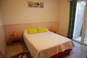 A bedroom with a bed, two bedside tables, a nightstand, a window with curtains, and a wall-mounted picture.