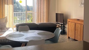 A modern living room with a round dining table, a sofa, a TV, and a balcony with curtains.
