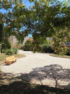 A gravel courtyard with a bench, surrounded by trees and shrubs.
