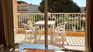 A balcony with a glass table and chairs, an orange striped umbrella, and a view of buildings and trees.
