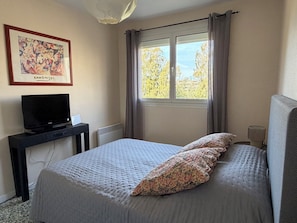 Une chambre à coucher avec un lit, une télévision, un bureau, un radiateur et une fenêtre avec des rideaux.