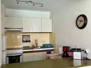 A kitchen with white cabinets, a stove, a sink, and a clock on the wall.
